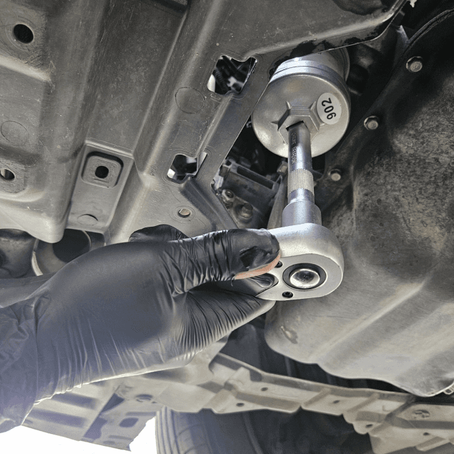 Gloved technician loosening the sump plug from underneath the car