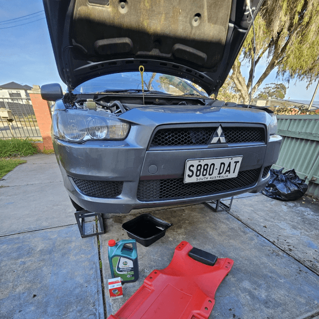 Mitsubishi Lancer up on ramps mid oil change, fresh oil and drain pan ready